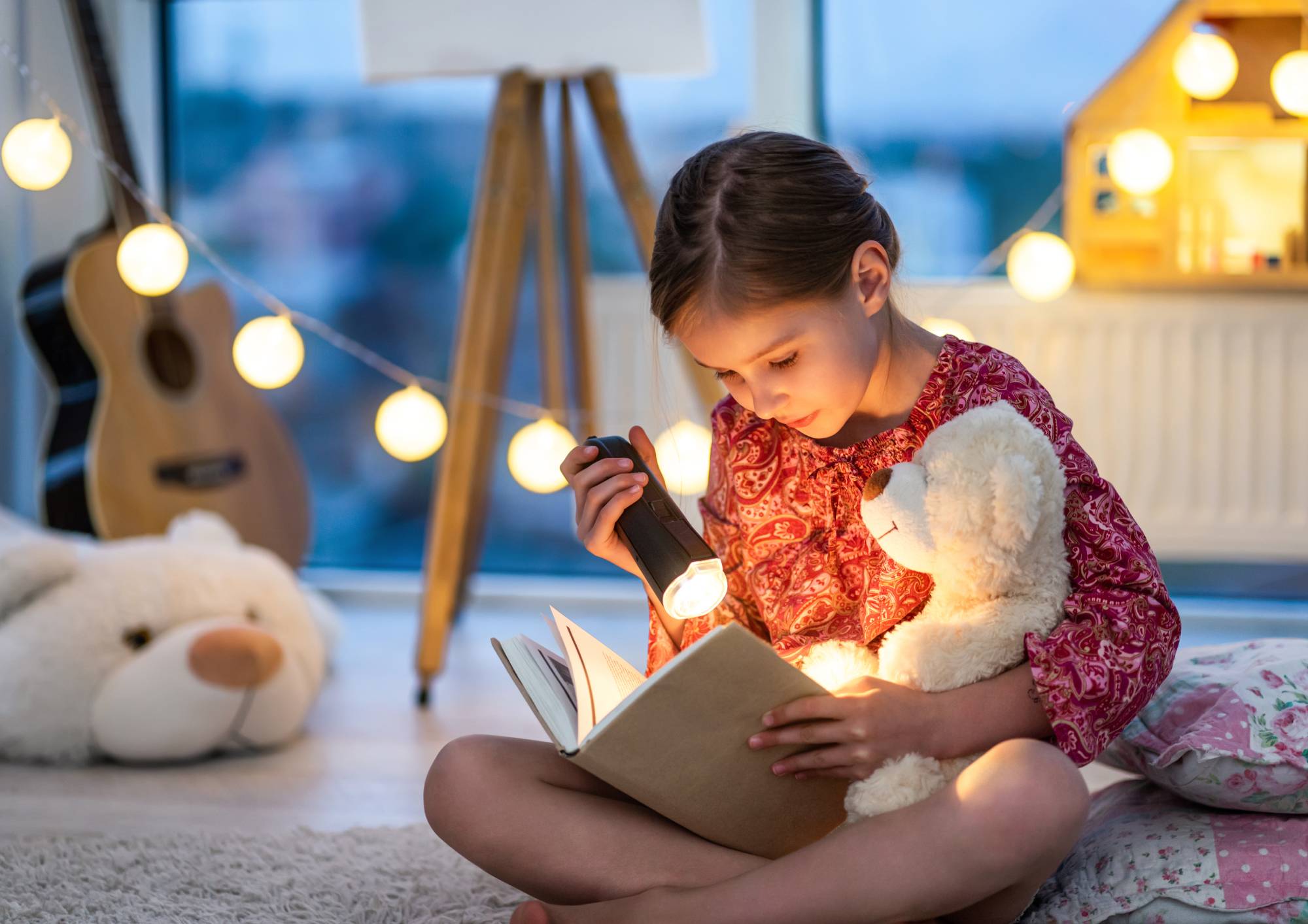 Dziecko czytające książkę przy włączonej lampce w pokoju