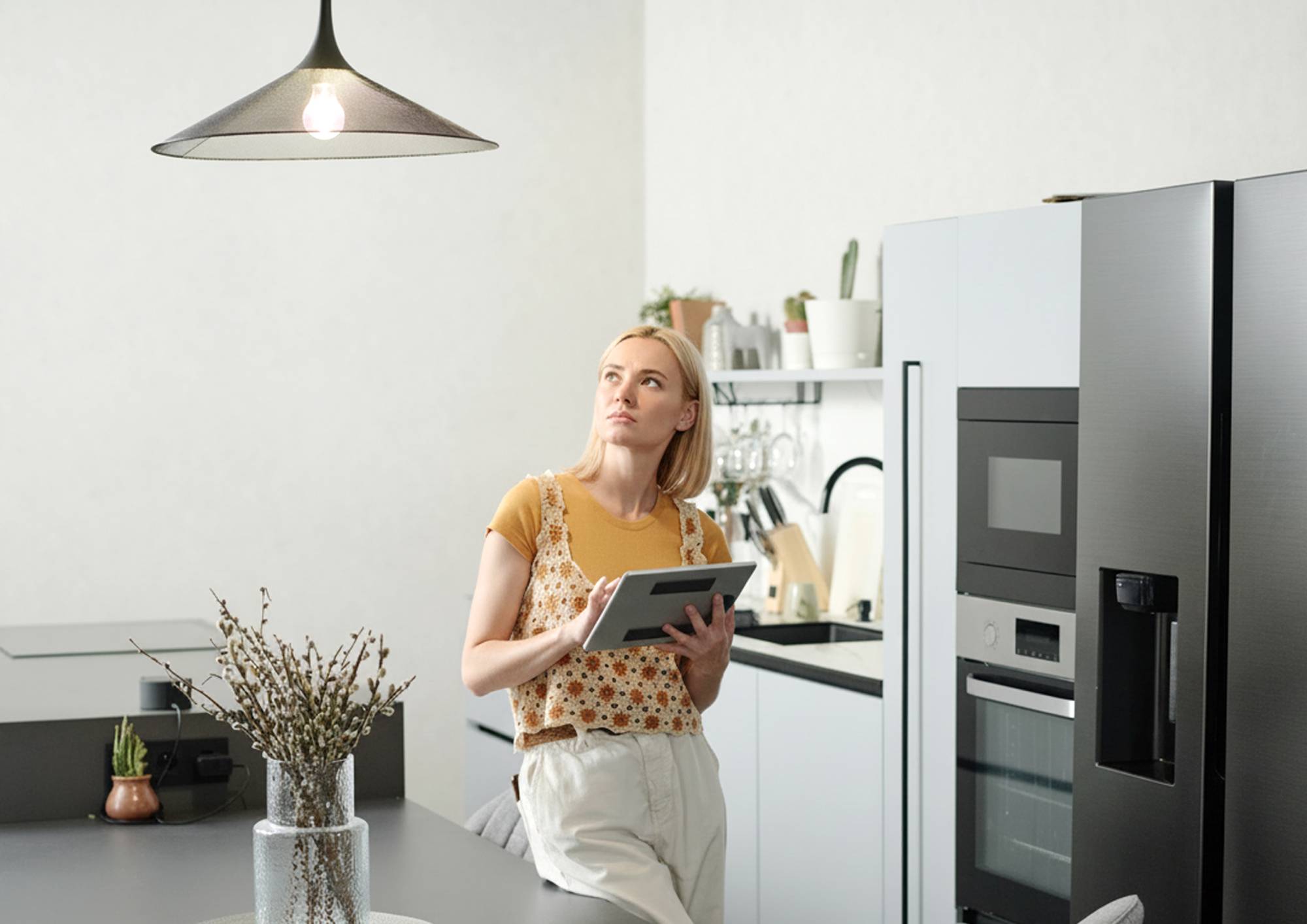 Kobieta stojąca w kuchni przy włączonej lampie wiszącej
