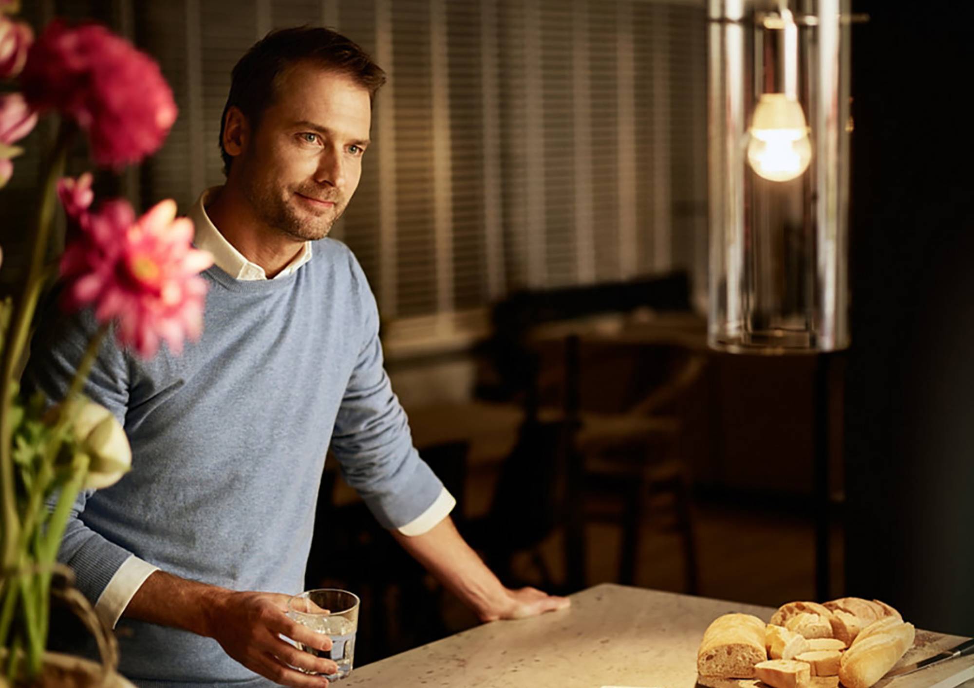 Mężczyzna stojący przy blacie kuchennym przy włączonej lampie wiszącej